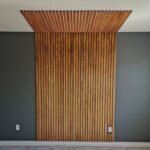 Vertical wooden slats forming an accent wall that extends onto the ceiling against a grey wall.