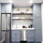 Small blue kitchenette with white countertops, stainless steel appliances, and wooden floating shelves on a white wall.