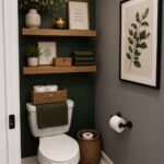Wooden floating shelves decorated with plants, candles, and framed art on a dark green bathroom wall.