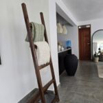 A wooden blanket ladder with green and white blankets draped over its rungs against a white wall.