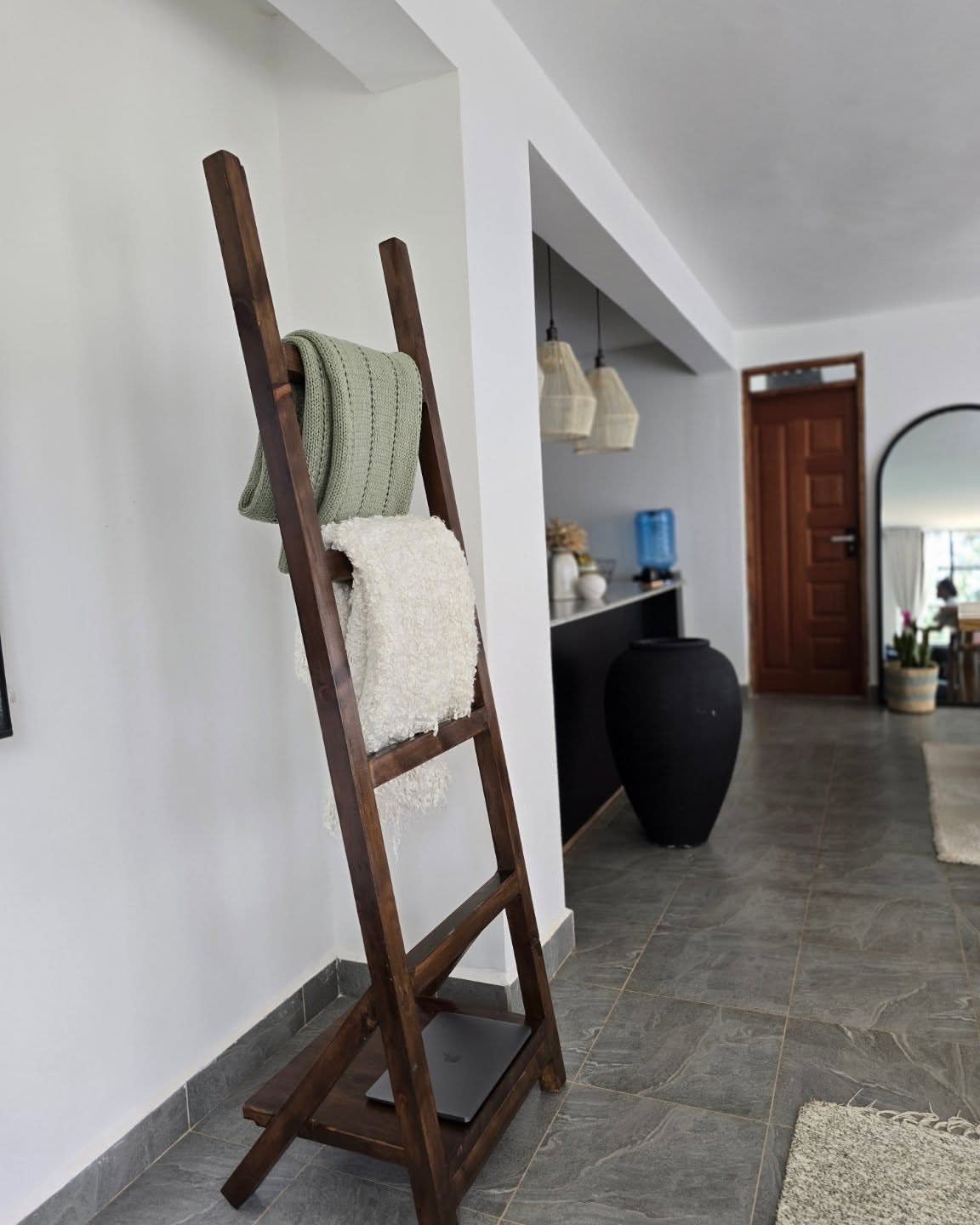 A wooden blanket ladder with green and white blankets draped over its rungs against a white wall.