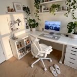 A minimalist white desk setup with a computer, office chair, plants, and organized shelving.