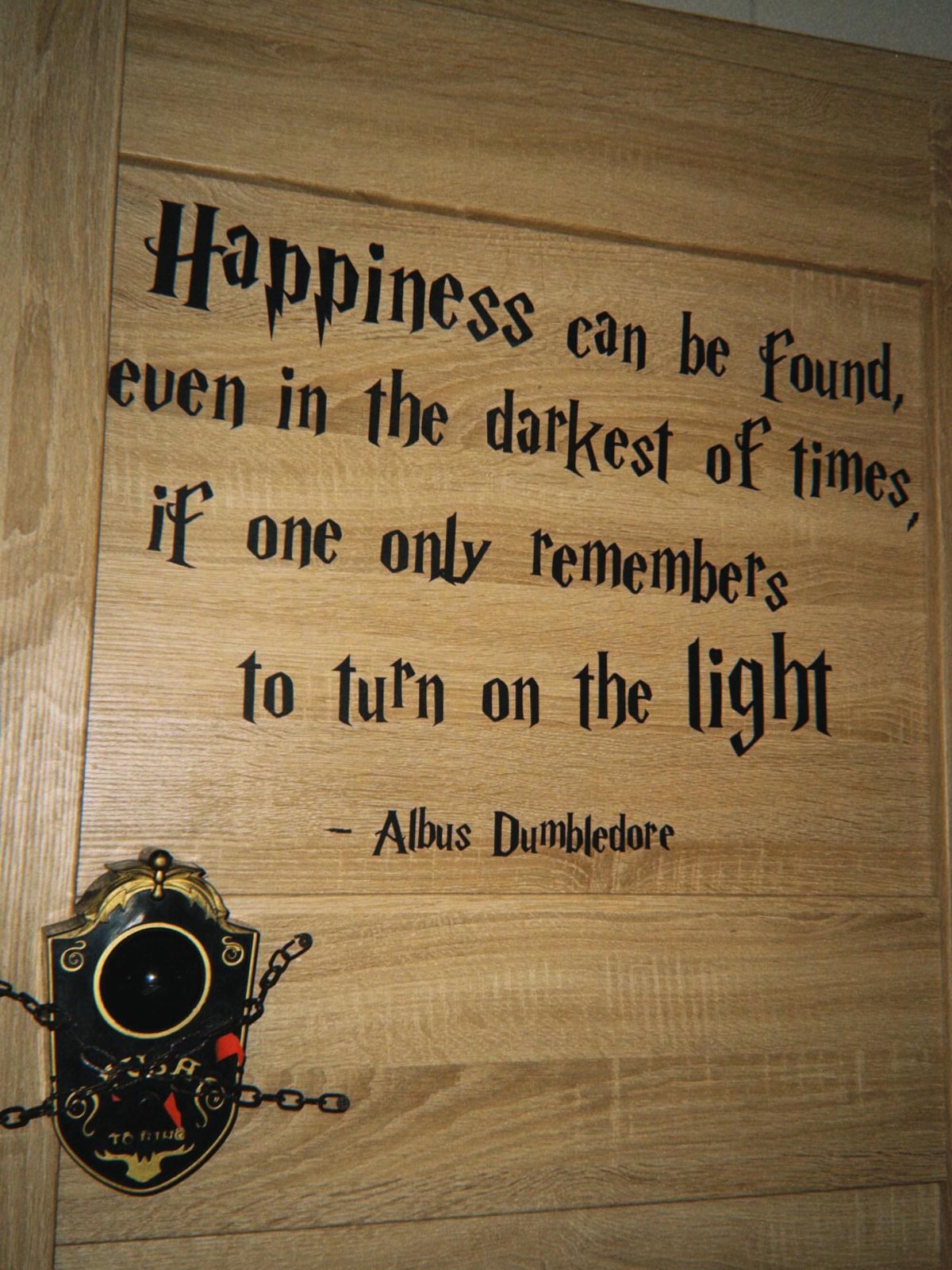 Wooden door with a printed Albus Dumbledore quote and a decorative shield-shaped doorbell.