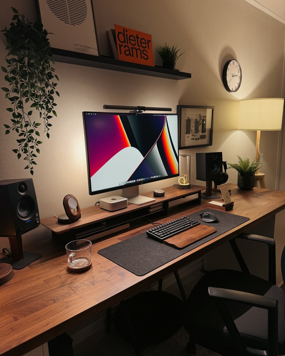 A wooden desk with a computer monitor, speakers, keyboard, and decorative plants in a home office.