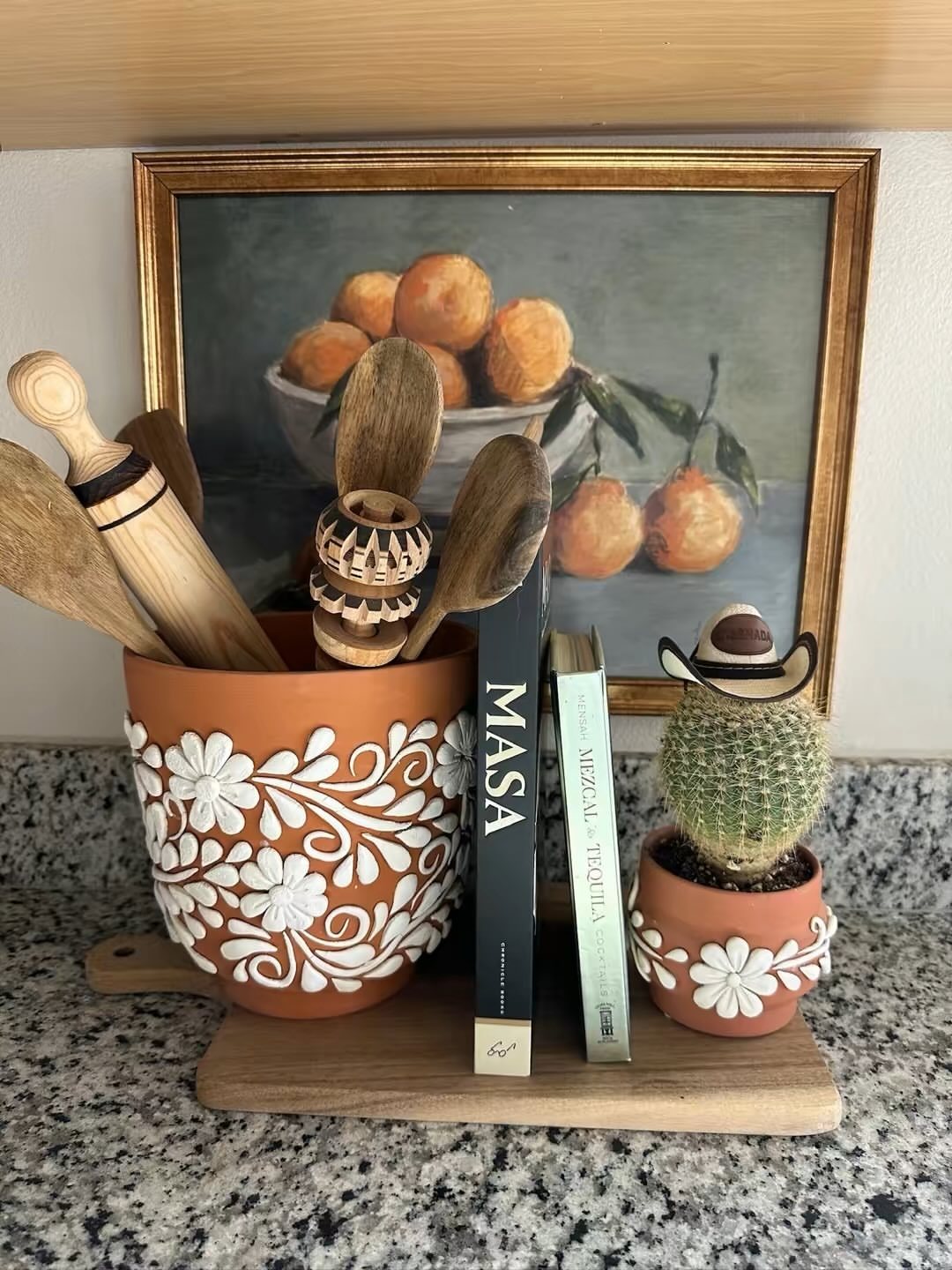 Terracotta pots with white floral designs holding wooden spoons and a small cactus on a wooden board.