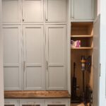 Grey built-in mudroom cabinetry with a wooden bench and an open storage closet containing a vacuum.