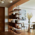 A dark wood open-shelf bookcase serving as a room divider in a modern dining room.